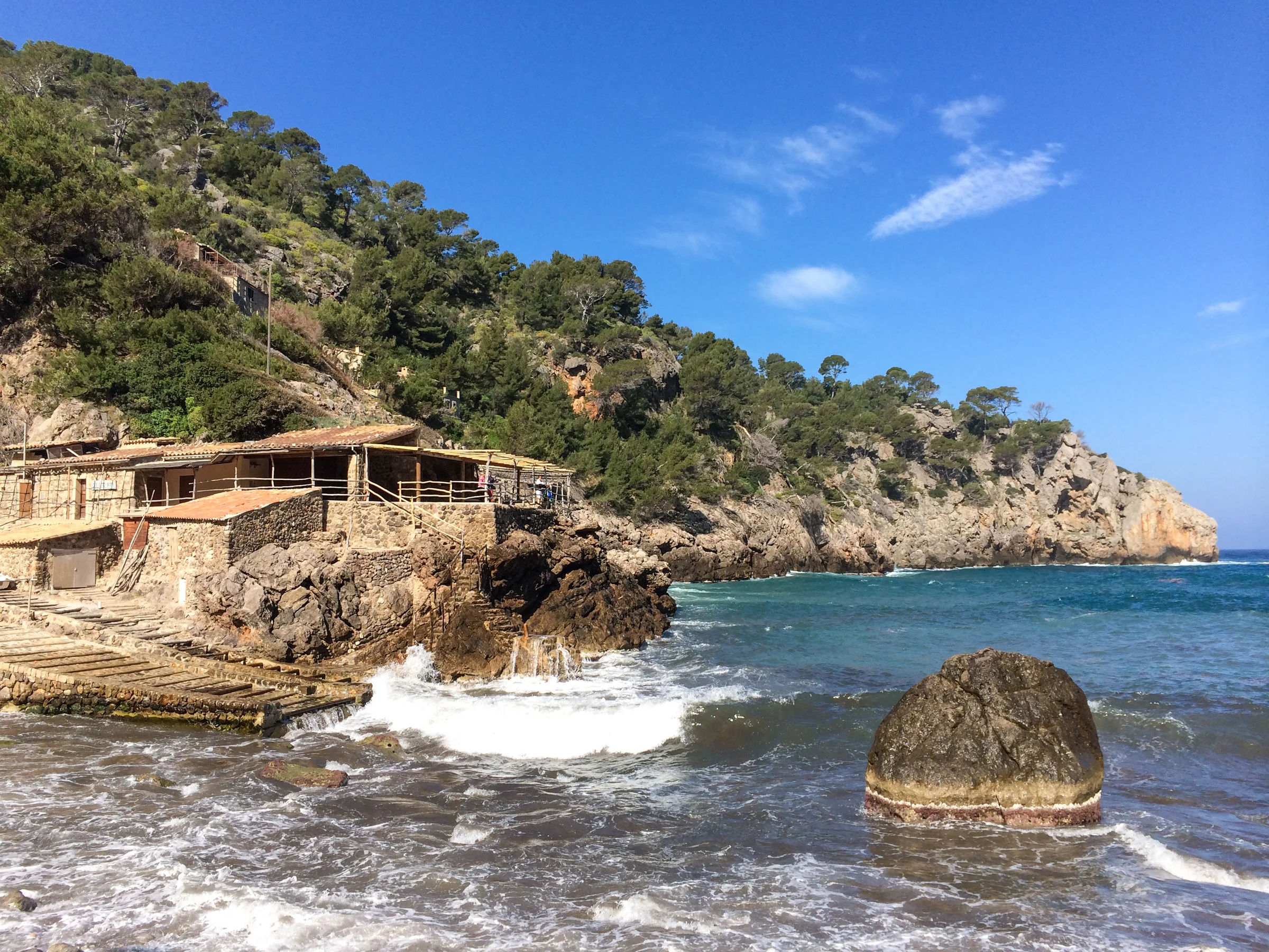 Stone buildings and pine-covered cliffs beside the sea at Cala Deià, Mallorca